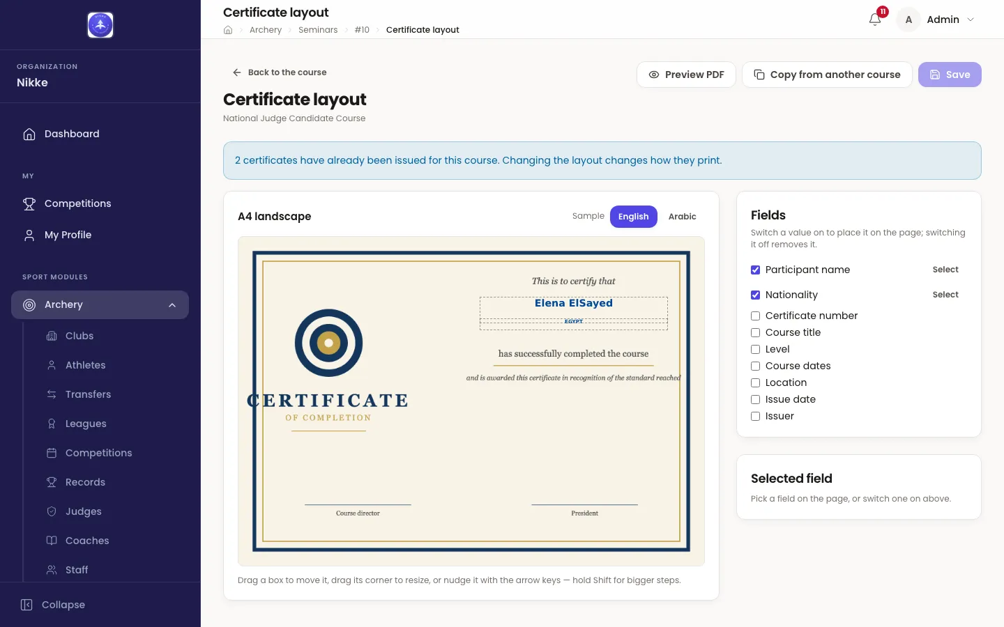 The Certificate layout page in Velos for the National Judge Candidate Course. At the top, a Back to the course link and three buttons: Preview PDF, Copy from another course and Save. A blue notice reads '2 certificates have already been issued for this course. Changing the layout changes how they print.' A card headed A4 landscape, with a Sample switch set to English beside Arabic, shows the course's certificate artwork — cream paper with a navy and gold border, a target emblem and the words CERTIFICATE OF COMPLETION in the left column — and two dashed boxes on it, the first reading Elena ElSayed in bold blue, the second EGYPT, between the artwork's 'This is to certify that' and 'has successfully completed the course'. Under the card: 'Drag a box to move it, drag its corner to resize, or nudge it with the arrow keys — hold Shift for bigger steps.' To the right, a Fields card lists nine checkboxes — Participant name and Nationality ticked with a Select link each, then Certificate number, Course title, Level, Course dates, Location, Issue date and Issuer — and a Selected field card says 'Pick a field on the page, or switch one on above.'