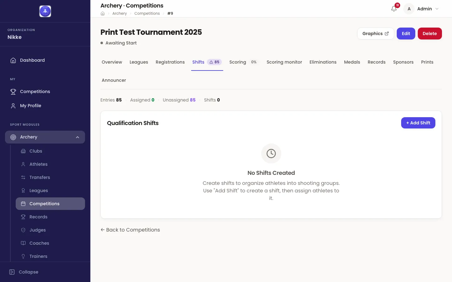The Shifts tab of the competition Print Test Tournament 2025 in Velos, marked Awaiting Start. A summary line reads Entries 85, Assigned 0, Unassigned 85, Shifts 0, and the Shifts tab itself carries a warning badge reading 85. Below it a card headed Qualification Shifts with a + Add Shift button holds an empty state reading No Shifts Created, over a line explaining that shifts organise athletes into shooting groups.